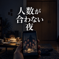 誕生日の後の暗い部屋と、余分な人影が写るスマートフォン。題名は人数が合わない夜。